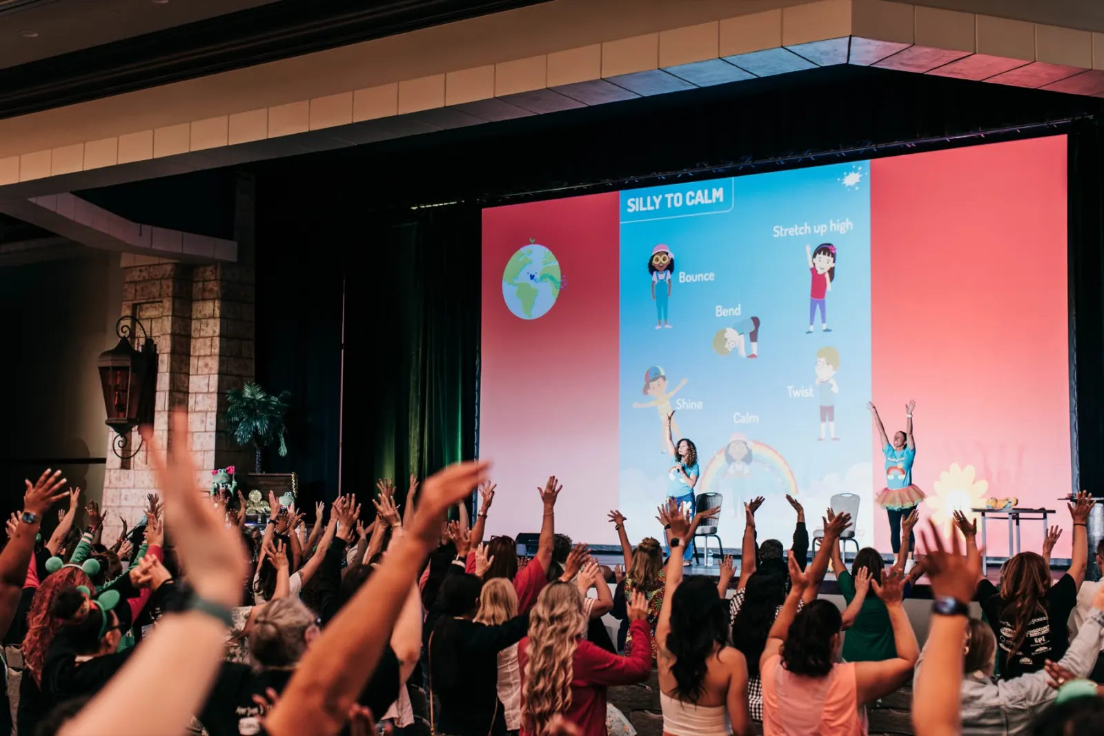 A full room of teachers raising their hands at a Yogapalooza session